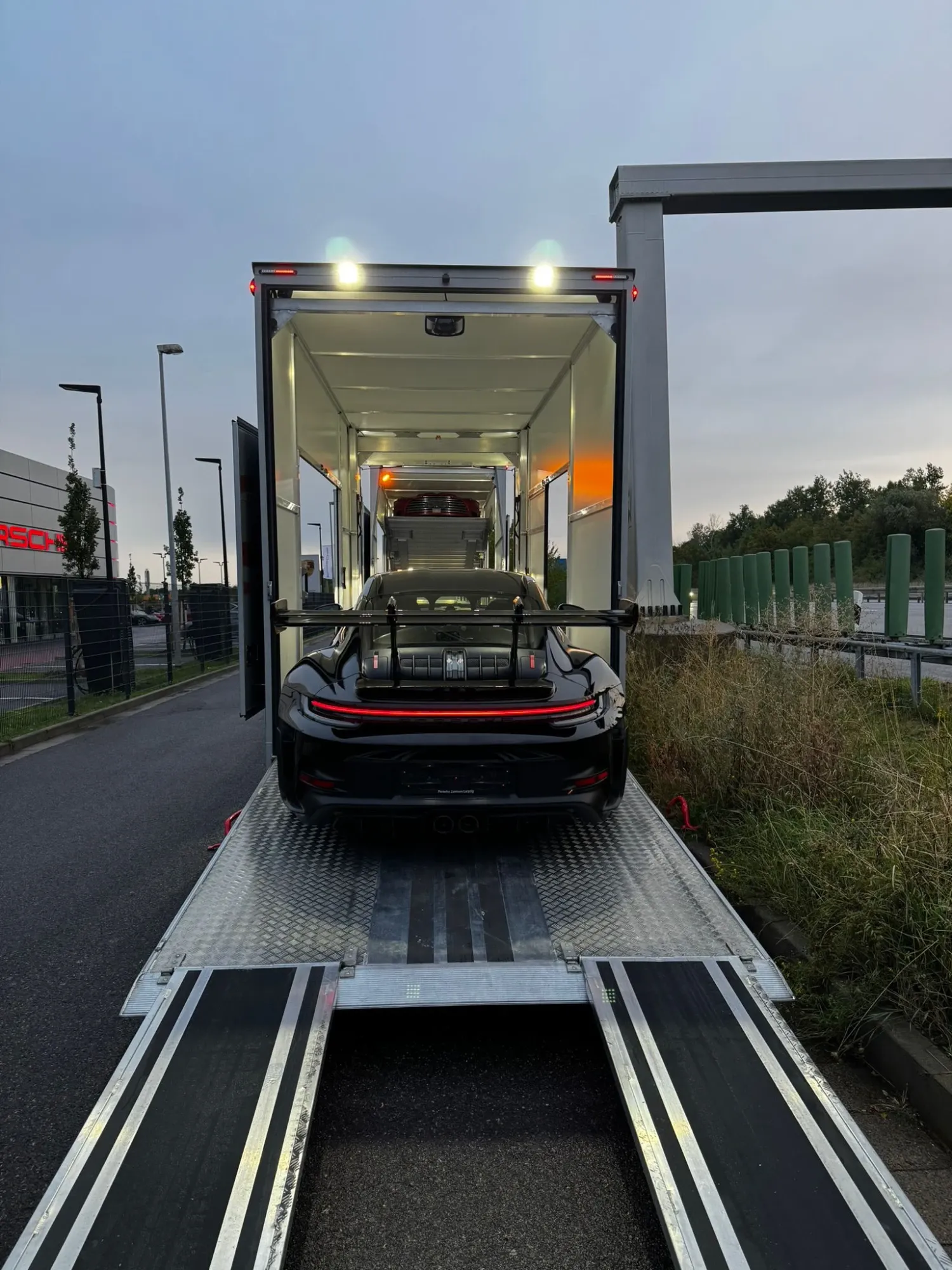 Zwarte Porsche 911 GT3 RS rijdt via de laadklep de gesloten trailer in
